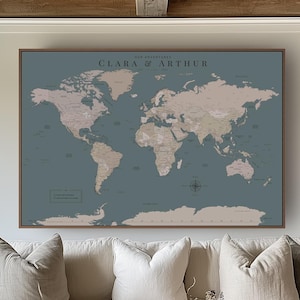 Peut inclure: Une grande carte murale rectangulaire présentant un fond bleu sourd avec des continents beiges. Le texte "THE ADVENTURES OF CLARA & ARTHUR" est imprimé en lettres sombres au centre supérieur. La carte est encadrée d'un fin cadre en bois brun.