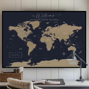 May include: A large rectangular wall map featuring a dark navy background with gold-coloured continents. The text at the top reads The Williams Adventures Around The World. The map is displayed in a frame above a desk with a chair and a desk lamp.