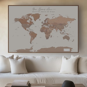 May include: A framed world map in shades of brown and tan, with the text "Your Names Here Adventures Around The World" in elegant script. The map is displayed above a white sofa and a rustic wooden coffee table, creating a warm, inviting atmosphere.