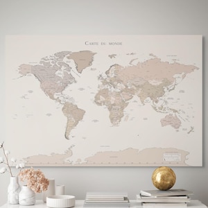 May include: A world map print with the text "CARTE DU MONDE" in black. The map is in neutral tones of beige, brown, and gray. The map is hanging above a white table with gold knobs, vases, and books.