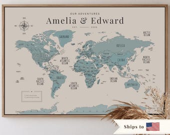 May include: A framed world map print with a beige background and blue-grey continents. The text reads Our Adventures, Amelia & Edward, and Est. 2020. It includes a compass rose, ocean labels, and a legend box in the lower left corner with two circles.