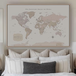Peut inclure: Une carte du monde encadrée aux tons neutres, représentant les continents et les pays. La carte comprend le texte "Our Adventures Around the World" et un logo pour Hilton & Co. La carte est affichée au-dessus d'un lit avec des oreillers décoratifs.
