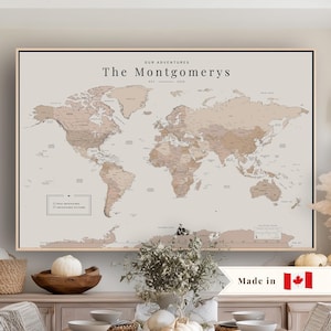 May include: A framed world map print in neutral beige and brown tones featuring the text Our Adventures, The Montgomerys, Est. 2020, and a legend with checkboxes for Past Adventures and Adventures to Come, displayed in a light wood frame.