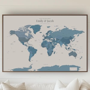 May include: A rectangular wall map featuring a world map in shades of blue against a light grey background. The text "OUR ADVENTURES" and "Emily & Jacob" is printed at the top centre. The map is enclosed in a thin, dark brown wooden frame.