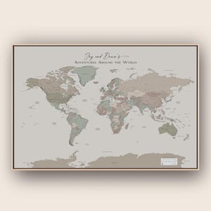 Peut inclure: Une carte du monde rectangulaire dans un cadre en bois fin, présentant des tons vert sauge et rose poudré sur un fond gris clair. Le texte "Jay and Dawn's ADVENTURES AROUND THE WORLD" est imprimé en noir en haut au centre en écriture cursive.
