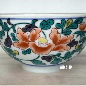 May include: White ceramic bowl with a floral design. The bowl features orange and yellow flowers, green leaves, and blue accents. The text "AIKA JP" is printed on the side of the bowl.