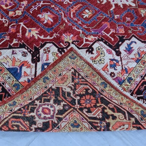 May include: Close-up of a corner of a red, blue, and cream colored rug with intricate floral and geometric patterns. The rug has a fringe border.