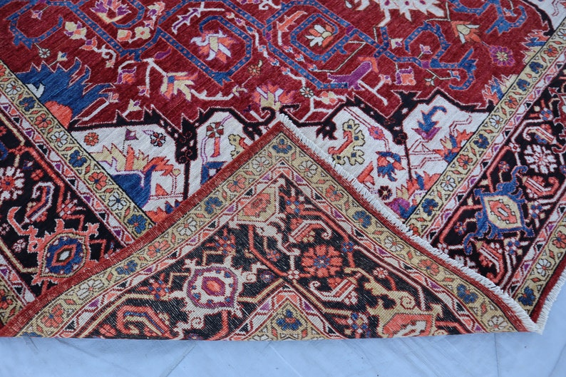 May include: Close-up of a corner of a red, blue, and cream colored rug with intricate floral and geometric patterns. The rug has a fringe border.
