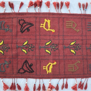 May include: A red wool runner rug with embroidered designs of birds, plants, and animals. The rug has a fringe border with tassels.