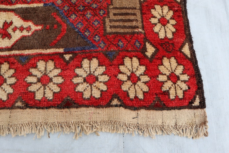 May include: Close-up of the bottom edge of a red, brown, and white patterned rug with a fringe. The rug has a floral design with white flowers on a red background.