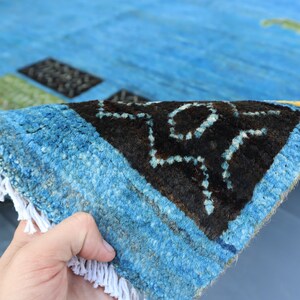 May include: Close-up of a blue and black patterned rug with white fringe. The rug is folded in half, showing the underside of the fabric.