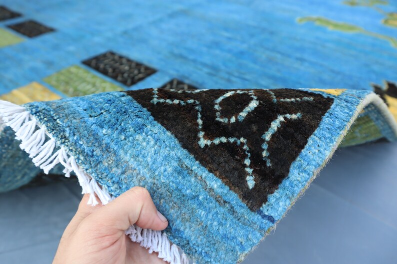 May include: Close-up of a blue and black patterned rug with white fringe. The rug is folded in half, showing the underside of the fabric.