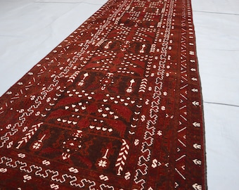 Puede incluir: Una alfombra larga y estrecha de color rojo y blanco con un patrón geométrico. La alfombra tiene un fondo marrón oscuro con diseños geométricos blancos.