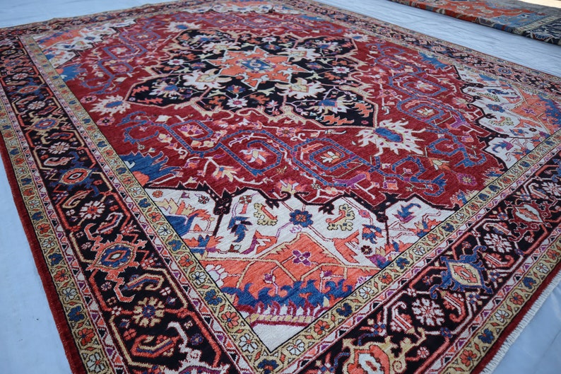 May include: A traditional Persian rug with a red background and intricate floral and geometric patterns in shades of blue, cream, and black. The rug has a central medallion and a border with a repeating design.