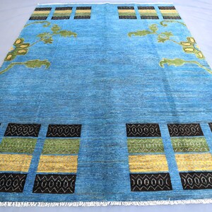 May include: A blue rug with a geometric pattern in black, yellow, and green. The rug has a fringe border.