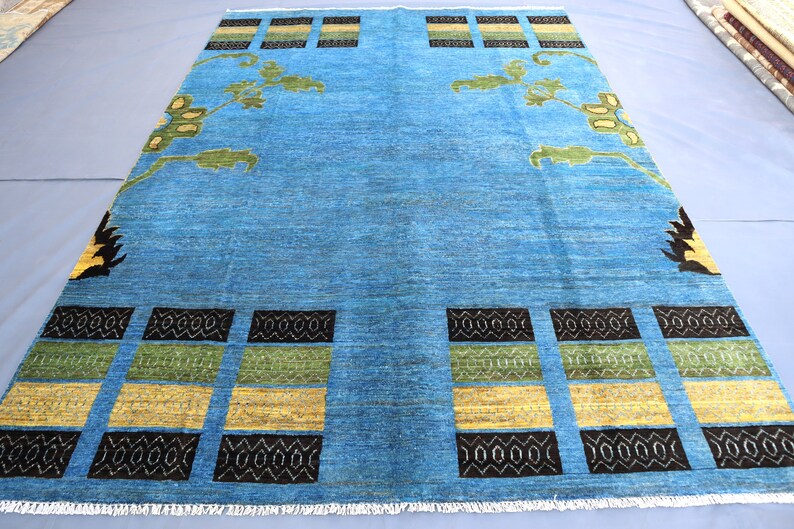 May include: A blue rug with a geometric pattern in black, yellow, and green. The rug has a fringe border.