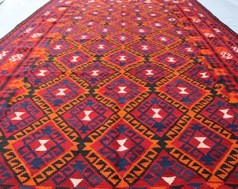 Puede incluir: Una alfombra rectangular con un patrón geométrico. La alfombra presenta un diseño de diamantes repetidos en rojo, naranja, azul marino, negro y blanco. La alfombra probablemente está hecha de tela tejida y es adecuada para cubrir el suelo.