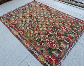Op de afbeelding: Een rechthoekig geweven vloerkleed met een herhalend ruitpatroon in tinten rood, groen, geel en blauw. Het kleed heeft een geometrisch ontwerp met kleine witte accenten in elke ruitvorm en is voorzien van korte franjes aan de randen.
