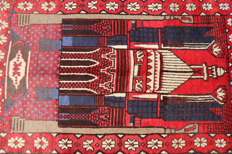 May include: A red prayer rug with a traditional Islamic design featuring a mosque and geometric patterns. The rug has a white border with floral motifs.