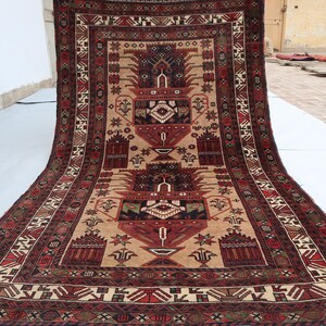 Pu&ograve; includere: Un tappeto tradizionale con sfondo beige e intricati motivi in rosso, nero e verde. Il tappeto presenta un disegno centrale con due grandi motivi floreali stilizzati.