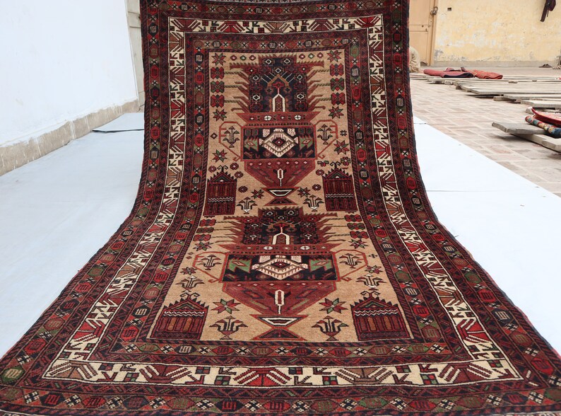 Pu&ograve; includere: Un tappeto tradizionale con sfondo beige e intricati motivi in rosso, nero e verde. Il tappeto presenta un disegno centrale con due grandi motivi floreali stilizzati.