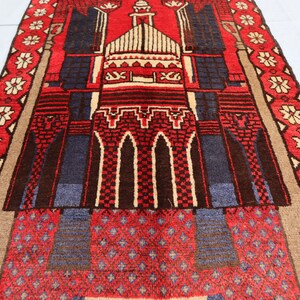 May include: A red, blue, and beige prayer rug with a mosque design. The rug has a geometric pattern and a floral border.