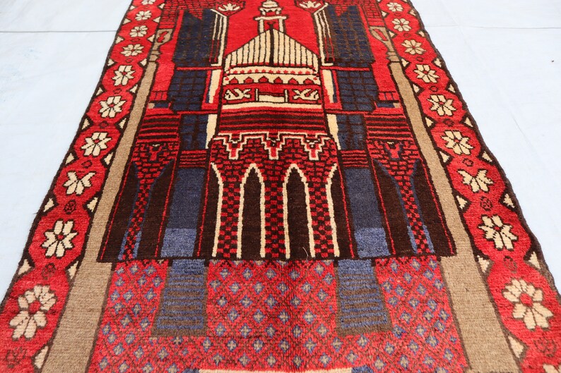 May include: A red, blue, and beige prayer rug with a mosque design. The rug has a geometric pattern and a floral border.