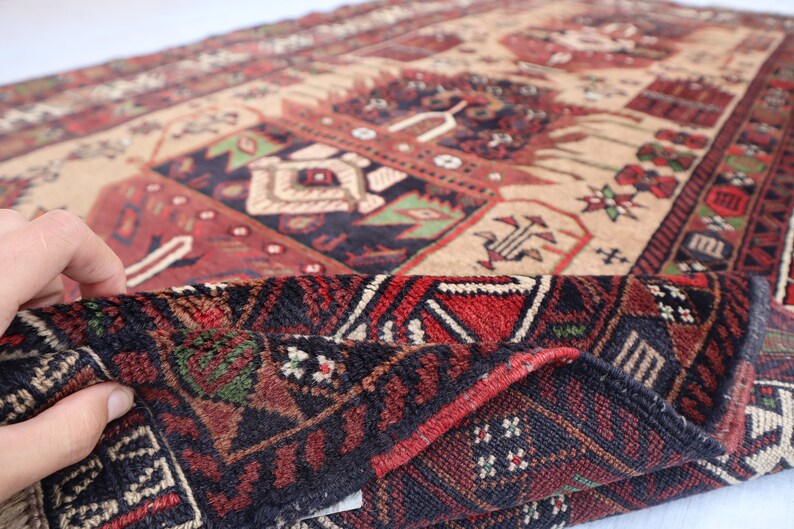 Pu&ograve; includere: Primo piano di un tappeto rosso, nero e crema con intricati motivi geometrici. Il tappeto &egrave; piegato a met&agrave;, rivelando il retro, che &egrave; di colore marrone scuro.