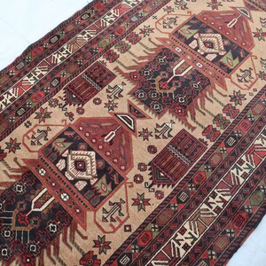 Pu&ograve; includere: Un tappeto tradizionale con sfondo beige e motivi intricati in tonalit&agrave; di rosso, nero e verde. Il tappeto presenta un disegno centrale con un motivo geometrico e un bordo con motivi ripetuti.