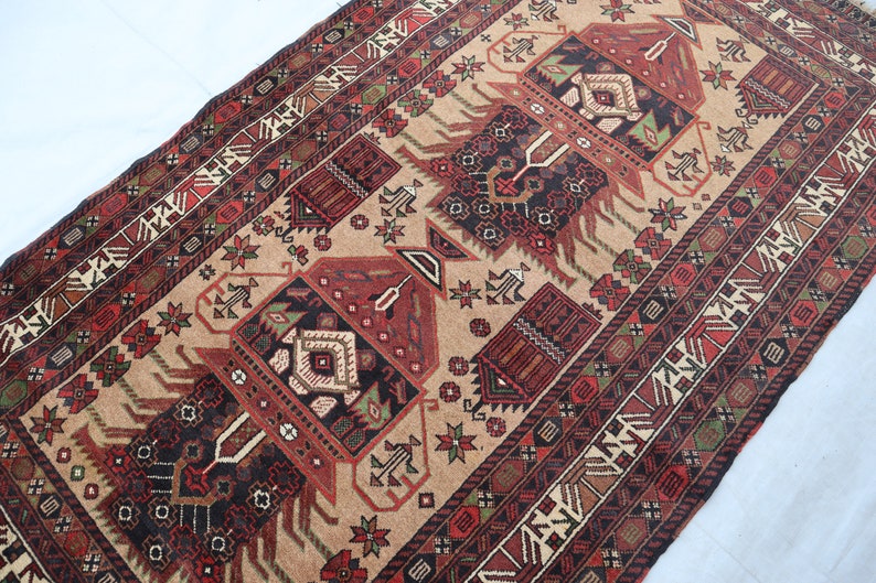 Pu&ograve; includere: Un tappeto tradizionale con sfondo beige e motivi intricati in tonalit&agrave; di rosso, nero e verde. Il tappeto presenta un disegno centrale con un motivo geometrico e un bordo con motivi ripetuti.