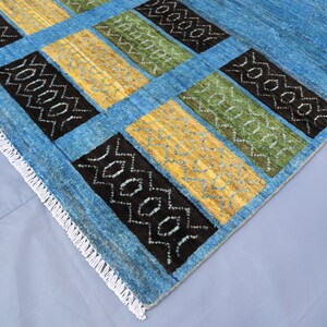 May include: A blue rug with a geometric pattern in black, yellow, and green. The rug has a white fringe border.