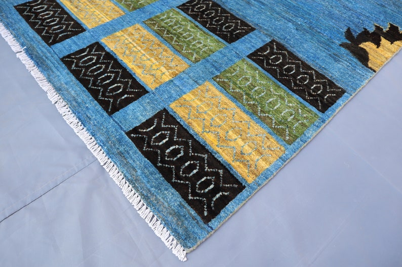 May include: A blue rug with a geometric pattern in black, yellow, and green. The rug has a white fringe border.
