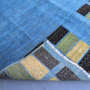 May include: A blue rug with a geometric pattern in black, yellow, and green. The rug has a fringe border.
