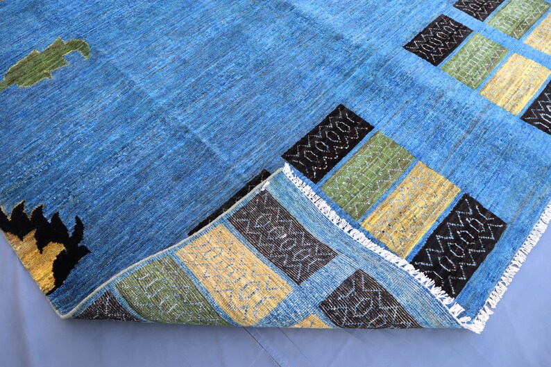 May include: A blue rug with a geometric pattern in black, yellow, and green. The rug has a fringe border.