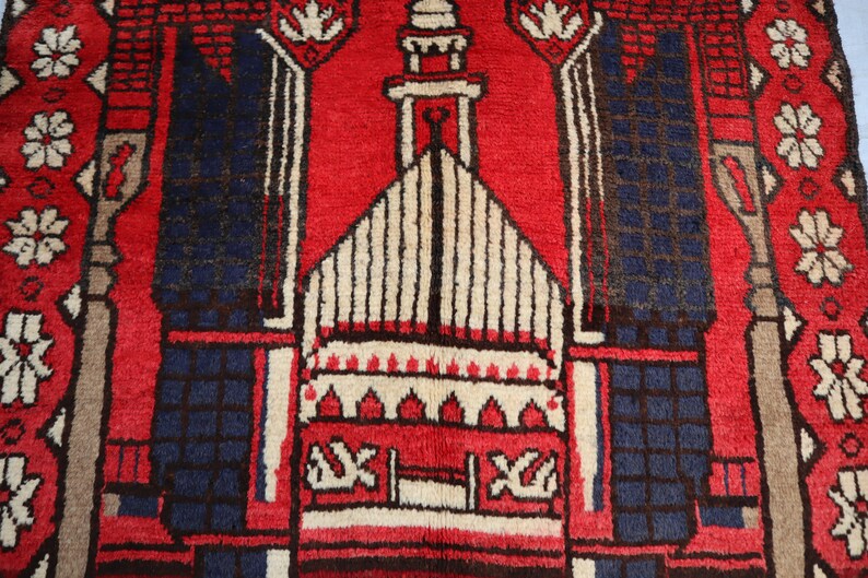 May include: A red prayer rug with a white and brown mosque design in the center. The rug has a blue border with white floral patterns.