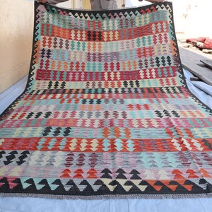 Puede incluir: Una alfombra tejida a mano colorida con un patrón geométrico en tonos de rojo, azul, verde y amarillo. La alfombra tiene un borde negro y está hecha de lana.