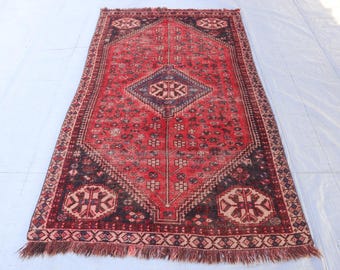 Puede incluir: Una alfombra vintage roja y negra con un patrón geométrico y flecos en los bordes. La alfombra tiene un aspecto descolorido y desgastado, lo que le da un carácter único.