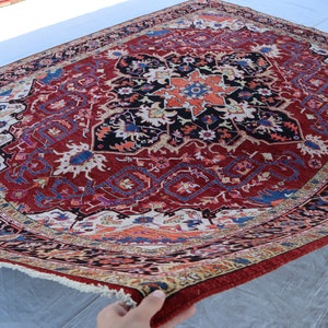 May include: A red, blue, and cream colored rug with a detailed floral pattern. The rug has a fringe border and is folded in half.