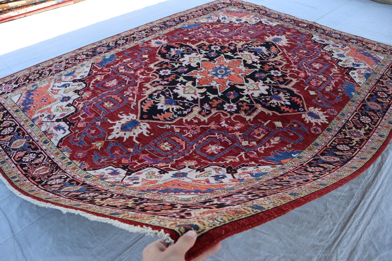 May include: A red, blue, and cream colored rug with a detailed floral pattern. The rug has a fringe border and is folded in half.