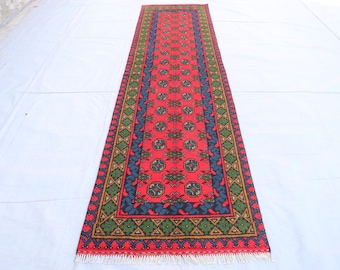 Puede incluir: Un tapete de corredor rojo, azul y verde con un borde de flecos. La alfombra tiene un diseño tradicional con formas geométricas y motivos florales.
