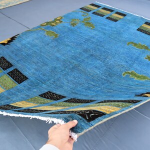 May include: A blue rug with a geometric pattern in black, yellow, and green. The rug has a fringe border and is folded in half.