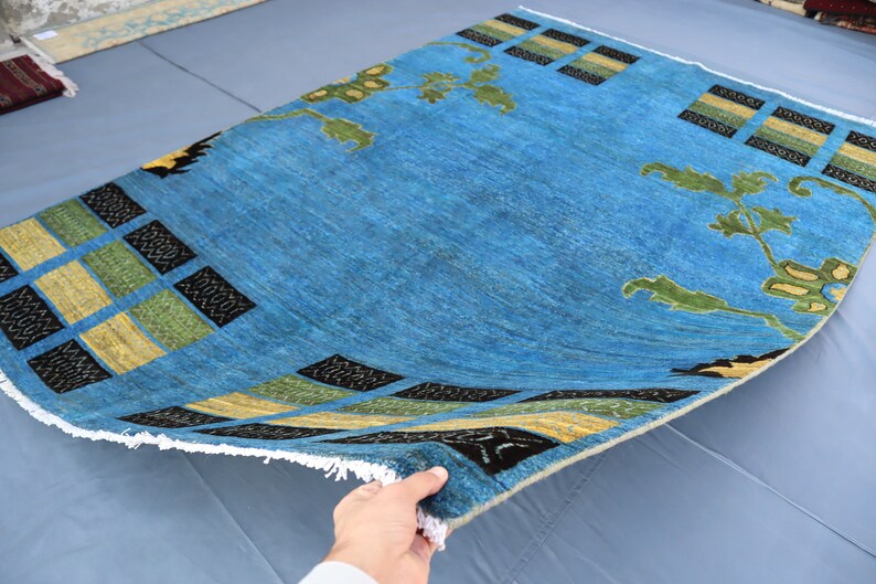 May include: A blue rug with a geometric pattern in black, yellow, and green. The rug has a fringe border and is folded in half.