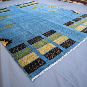 May include: A blue rug with a geometric pattern of black, yellow, and green squares. The rug has a white fringe border.