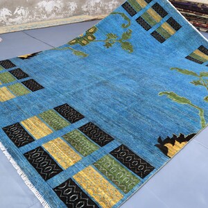 May include: A blue rug with a geometric pattern of black, yellow, and green squares. The rug has a fringe border and features a floral design in the center.