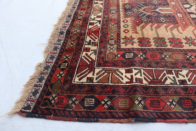 Pu&ograve; includere: Un tappeto tradizionale con sfondo beige e intricati motivi geometrici in tonalit&agrave; di rosso, marrone, verde e nero. Il tappeto ha un bordo con frange.