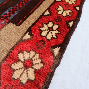 May include: Close-up of a red, brown, and cream-colored rug with a floral pattern. The rug has a fringe border.