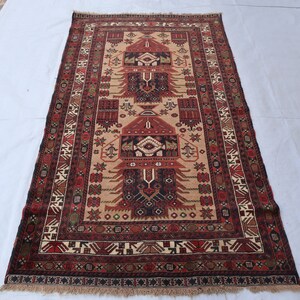 Pu&ograve; includere: Un tappeto tradizionale con sfondo beige e intricati motivi in rosso, nero e verde. Il tappeto presenta un disegno centrale con un motivo ripetitivo di alberi stilizzati e forme geometriche.
