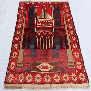 May include: A red and blue prayer rug with a mosque design and floral border. The rug has a fringed edge.