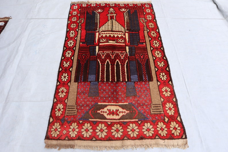 May include: A red and blue prayer rug with a mosque design and floral border. The rug has a fringed edge.