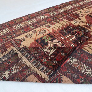 Pu&ograve; includere: Un tappeto tradizionale con sfondo beige e motivi intricati in tonalit&agrave; di rosso, nero e verde. Il tappeto ha un bordo con frange ed &egrave; piegato a met&agrave;.
